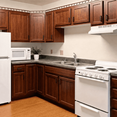 A kitchen with wooden cabinets, a white microwave on the countertop, a potted plant, a white refrigerator, a stainless steel sink, and a white stove with an oven.